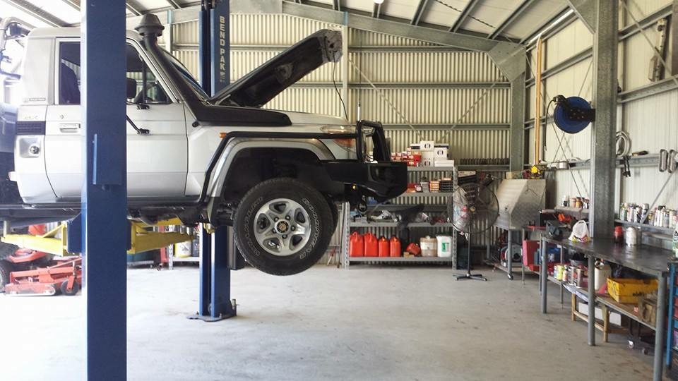 A Toyota Landcruiser ute raised on the two post hoist inside the Mossman Mechanical workshop, bonnet open