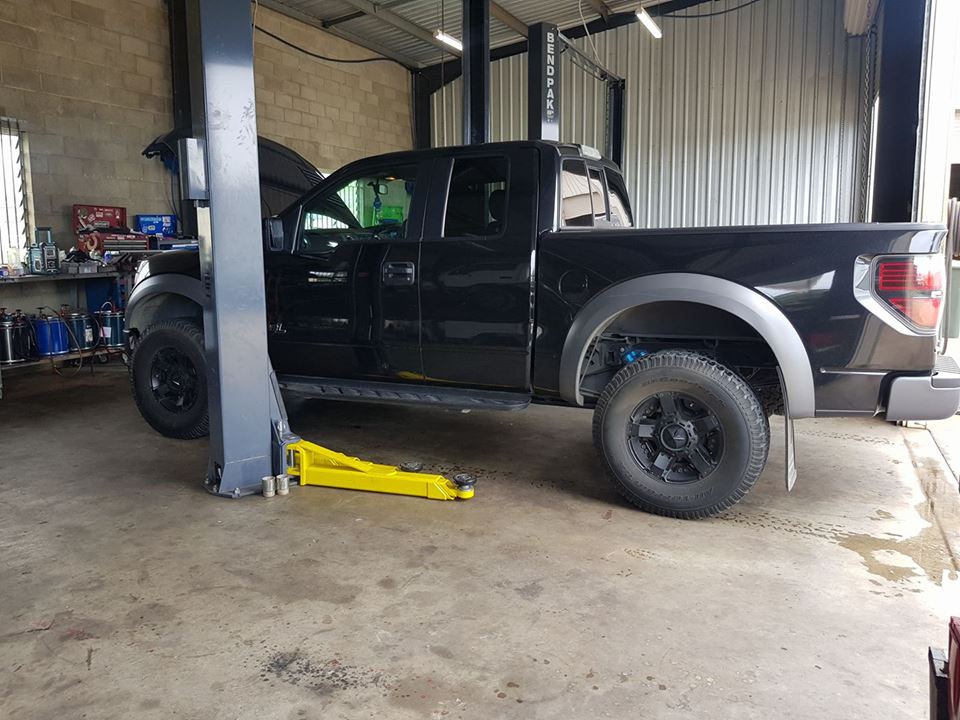 A black Ford F-150 Raptor in the workshop with the front wheel off and a trolley jack underneath